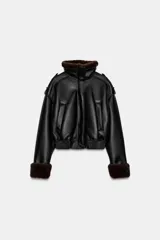 Cazadora bomber de efecto piel en color negro, con cuello subido, manga larga y bajo elástico. Presenta interior y puños con aplicación de pelo sintético en color marrón a contraste, cierre frontal con cremallera y botones a presión, y bolsillos laterales de vivo.