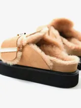 Zueco negro de cuero con plataforma y plantilla recubierta de piel de oveja. Presenta una hebilla dorada de gran tamaño en la capellada.