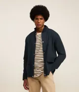 Campera bomber azul marino para hombre, confeccionada en sarga de algodón sostenible. Tiene cuello alto, cierre abotonado, bolsillos cargo con solapa y puños elásticos.