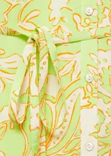 Vestido corto de tejido fluido con estampado paisley en tonos verde lima y crema. Presenta escote en pico, cierre frontal con botones, mangas tres cuartos con puños elásticos y falda con detalle de volante en el bajo. Incluye un cinturón fino del mismo tejido para ajustar a la cintura.