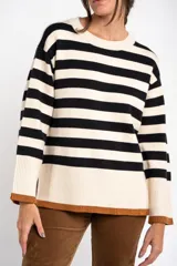 Sweater de punto con diseño a rayas horizontales en color negro y crema, de corte oversize. Presenta cuello redondo, mangas largas con puños acanalados y un detalle de borde inferior en color cobre con acabado brillante.