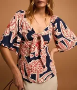 Blusa azul marino con estampado floral en tonos rojo y blanco, escote en pico con nudo y mangas cortas fruncidas.