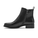 Bota corta de cuero negro con cierre lateral metálico que incluye un dije circular con la letra K. Presenta un diseño minimalista con taco bajo cuadrado y suela de goma.