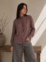 Camisa de manga larga color blanco, con cuello alto y detalle de volados en el cuello y a lo largo de la botonadura frontal. Presenta puños con volados y cierre de botones.
