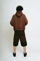 Bermuda de jean color marrón oscuro con efecto lavado, corte baggy y largo hasta la rodilla. Presenta bordados ornamentales en color crema/dorado en los bajos de ambas piernas.
