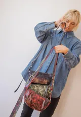 Bandolera de cuero color rojo con detalles en negro, con correa regulable y cierre superior con cremallera.