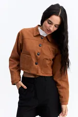 Campera corta tipo gamuza con textura suave y acabado mate. Presenta cuello camisero, cierre frontal con botones oscuros y dos bolsillos frontales de parche. Su diseño es de silueta cropped.