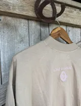 Remera de manga corta y cuello redondo, color beige claro, con un bordado central que representa el Sol de Mayo con el texto "REPUBLICA ORIENTAL DEL URUGUAY" y "EST. 1825".