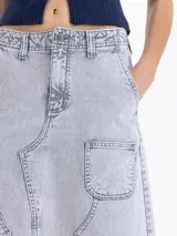 Pollera midi de denim en color azul claro con efecto lavado. Presenta un diseño de corte recto con costuras decorativas visibles, bolsillos frontales tipo cargo y una abertura central en el ruedo.