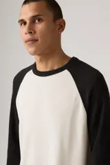 Remera térmica de manga larga con diseño raglán, color blanco en el cuerpo y negro en las mangas. Presenta un tejido texturizado tipo waffle y cuello redondo.