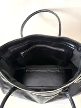 Bolso grande de cuero marrón con textura tipo cocodrilo, estructura rígida y asas para llevar al hombro. Tiene una tira con tachas y hebillas en cada extremo, también lleva lazos en los costados.