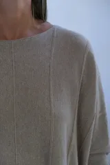 Sweater de punto con acabado brillante, color visón, de corte holgado y mangas largas con puños ajustados. Presenta un diseño con costuras verticales decorativas en el frente.