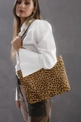Cartera tipo tote bag de tamaño pequeño, confeccionada en cuero con estampado animal print. Presenta detalles en cuero color chocolate en las manijas y terminaciones internas. Incluye cierre metálico superior para mayor seguridad.