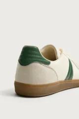 Zapatillas de estilo retro para hombre, color blanco off-white con detalles en verde oscuro y suela de goma marrón estilo gum. Presenta cordones al tono, refuerzos en gamuza en la puntera y talón, y bandas laterales verdes en contraste.