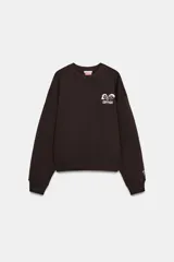 Sudadera de cuello redondo y manga larga con hombro caído, confeccionada en mezcla de algodón. Presenta un diseño liso en color marrón oscuro con un pequeño estampado gráfico a contraste en el pecho y detalle en el puño.