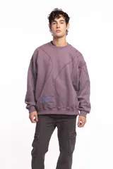 Buzo blanco de manga larga con diseño holgado, cuello redondo y costuras externas visibles en contraste. Cuenta con una etiqueta decorativa en el frente inferior.