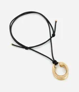 Collar corto con cordón negro ajustable y un colgante circular grueso en tono dorado. El diseño destaca por su aro de metal reciclado con acabado brillante.