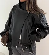 Campera de cuero sintético negro con diseño oversize, cuello alto, cierre frontal con cremallera y botones a presión, y cinturón ajustable en el ruedo.