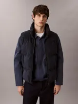 Chaleco acolchado reversible Calvin Klein, con diseño sin mangas, cuello alto y cierre frontal de cremallera. Presenta un lado de pana y otro de nailon liso.