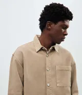 Camisa de sarga de algodón con acabado cationizado que le otorga un aspecto ligeramente desgastado. Presenta un corte boxy amplio, cuello clásico, cierre frontal con botones y un bolsillo aplicado en el pecho.