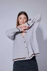 Saco tejido en lambswool con diseño de rombos y trenzas en el frente. Presenta cierre frontal con botones, cuello en V y detalles de rayas en contratono en puños y ruedo. Incluye pin bordado en la manga.
