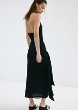 Vestido largo negro de corte slim, con cuello drapeado, sin mangas y detalle de fruncido lateral con caída de tela en la cadera.