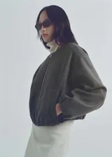 Chaqueta tipo bomber de color gris oscuro, con cuello redondo, cierre frontal de cremallera y diseño oversize. Presenta mangas largas con puños elásticos fruncidos y detalle fruncido en el bajo, además de dos bolsillos laterales.