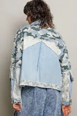 Chaqueta de denim de corte holgado y manga larga, con diseño en técnica de patchwork que combina sectores de mezclilla clásica, estampa de camuflaje, parches florales y detalles de encaje blanco. Cuenta con cierre frontal de cremallera metálica y cuello camisero.