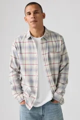 Camisa de manga larga con diseño a cuadros en tonos beige, azul y rojo. Presenta cuello clásico, cierre frontal con botones y un bolsillo en el pecho con etiqueta roja distintiva.