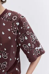 Remera de corte oversize color marrón con estampado tipo bandana en color blanco. Presenta cuello redondo y mangas cortas amplias.