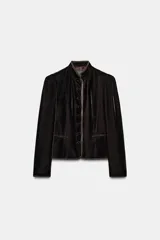 Blazer de terciopelo en color rosado con cuello subido y manga larga. Presenta cierre frontal con botones forrados y detalles de vivo en color oscuro a contraste en los bordes, cuello y puños. Incluye bolsillos delanteros de vivo.