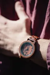 Reloj de pulsera con caja, esfera y malla de madera de sándalo rojo, con marcadores y manecillas negras. Presenta un diseño circular con corona lateral.