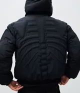 Campera puffer negra con diseño acolchado que simula una estructura de esqueleto. Cuenta con capucha, cierre frontal con cremallera, mangas largas y puños elásticos.