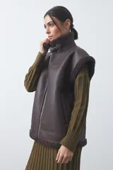 Chaleco de cuero sintético negro con interior y detalles de corderito en cuello, sisas y ruedo. Presenta cierre frontal completo y diseño holgado.