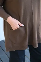 Sweater de tejido de punto en color chocolate, con corte holgado, cuello redondo y mangas largas. Presenta un diseño con bolsillos frontales integrados y terminaciones acanaladas en puños y ruedo.