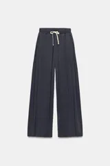 Pantalón de algodón color gris oscuro con efecto lavado, de tiro medio y cintura elástica ajustable con cordón crudo. Presenta bolsillos laterales ocultos, pliegues delanteros y diseño de pierna ancha.