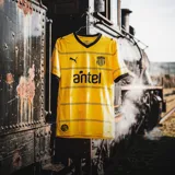 Camiseta de fútbol Puma del Club Atlético Peñarol, modelo Away Jersey. Diseño amarillo con cuello en V y detalles en negro en el cuello y las mangas. Incluye logo de Puma, escudo del club y sponsor Antel en el frente.