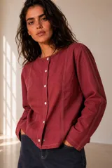 Chaqueta de lino color beige, de corte recto, escote redondo y cierre frontal con broches a presión. Cuenta con mangas largas y costuras decorativas pespunteadas en el frente.
