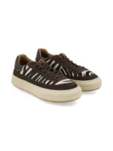 Sneaker de diseño urbano con combinación de cuero marrón y paneles de pelo con estampado animal print tipo cebra. Cuenta con suela de plataforma en tono crema y cordones al tono.