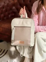 Mochila de cuero en color crudo, con bolsillo frontal con cierre y detalle de textura grabada. Cuenta con tiras ajustables y manija superior.