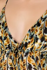 Vestido largo con estampado de hojas en tonos ocre, negro y blanco. Presenta escote en V profundo con ajuste de cordón bajo el busto, tirantes delgados ajustables y abertura frontal en la falda.