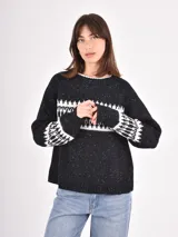 Buzo de tejido de punto en color negro con efecto jaspeado y diseño geométrico en blanco en la parte superior del pecho y en los puños. Presenta cuello redondo y mangas largas con terminaciones en tejido acanalado.