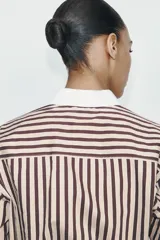 Camisa de manga larga con estampado de rayas verticales en tonos marrón y beige. Presenta cuello solapa y puños anchos en color blanco a contraste, con cierre frontal de botones.