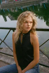 Top chaleco negro satinado con cuello halter, espalda descubierta y cierre frontal con cremallera y botón a presión ocultos por solapa.