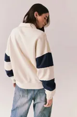 Sweater de algodón color beige claro con cuello polo y cierre frontal parcial. Presenta mangas largas con franjas horizontales azul marino y un estampado frontal con estrellas y la leyenda 'CALIFORNIA'.