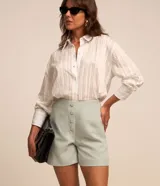 Short de sastrería color rosado, de tiro alto con detalles de pinzas frontales y cartera abotonada con cuatro botones revestidos. Presenta diseño recto y estructurado.