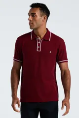 Chomba de piqué color bordó con detalles de ribetes blancos en cuello y mangas. Presenta cierre frontal de tres botones y logo de pingüino bordado en el pecho.