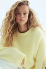 Buzo de punto suave color amarillo pálido, con textura afelpada, cuello redondo y mangas largas de corte amplio.