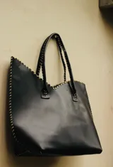 Cartera de cuero color marrón chocolate con manijas largas y borde superior en corte en V. Diseño amplio y liviano, con terminaciones artesanales y costuras contrastantes en todo el contorno.