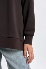 Buzo deportivo de corte oversize en color marrón, con cuello redondo y mangas largas tipo raglán. Presenta una estampa frontal con la inscripción 'Health Club' en tipografía cursiva y detalles de texto en blanco.